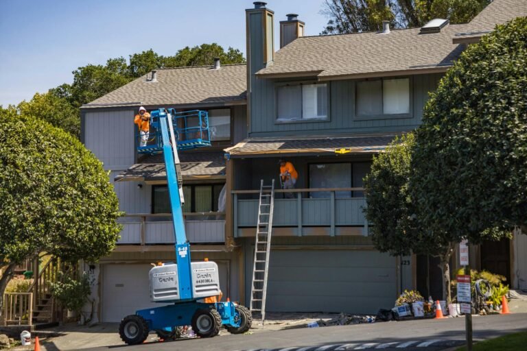 Two workers on a boom lift performing exterior siding installation on a residential house
