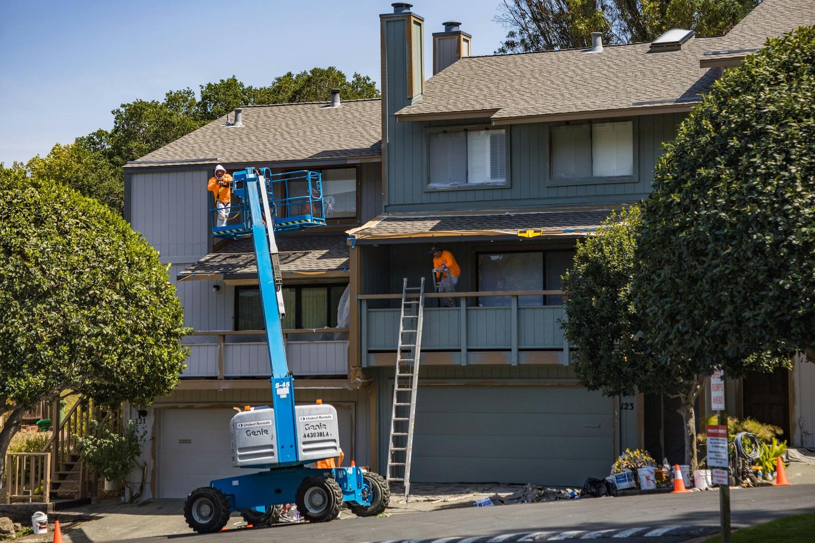 Two workers on a boom lift performing exterior siding installation on a residential house