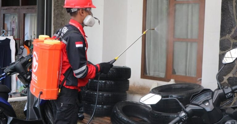 Pest control technician in protective suit spraying treatment on equipment